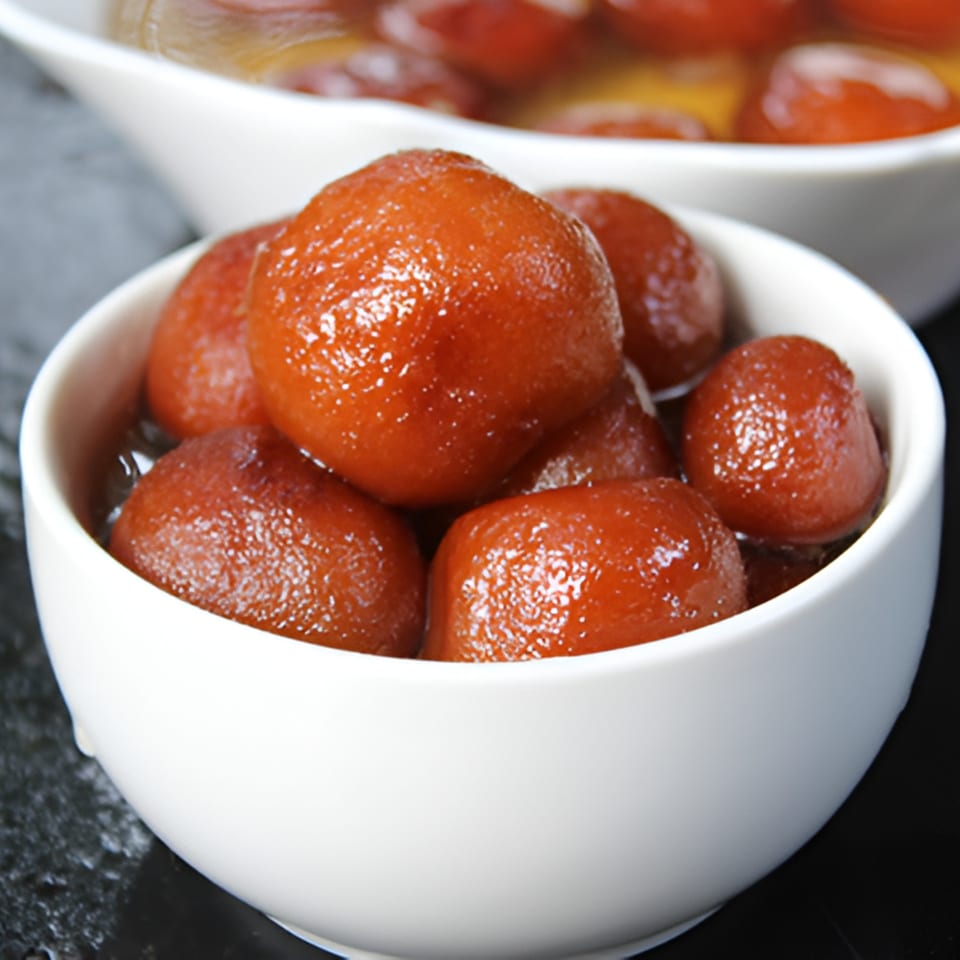 Two white bowls filled with glistening, syrup-soaked gulab jamun, an Indian dessert.