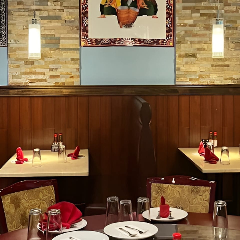 Taste of Awadh restaurant interior with set tables, red napkins, and a framed Indian art piece.