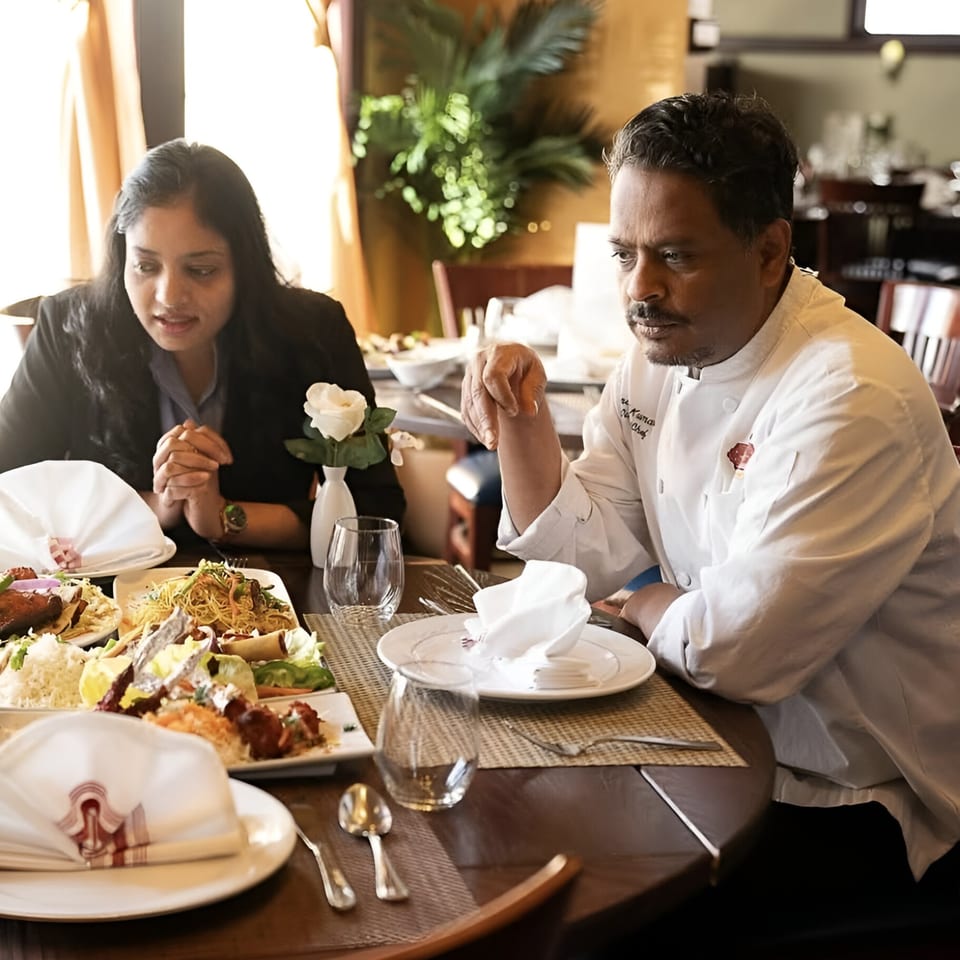 Chef Anand and a woman seated at a table with various Indian dishes at Taste of Awadh.