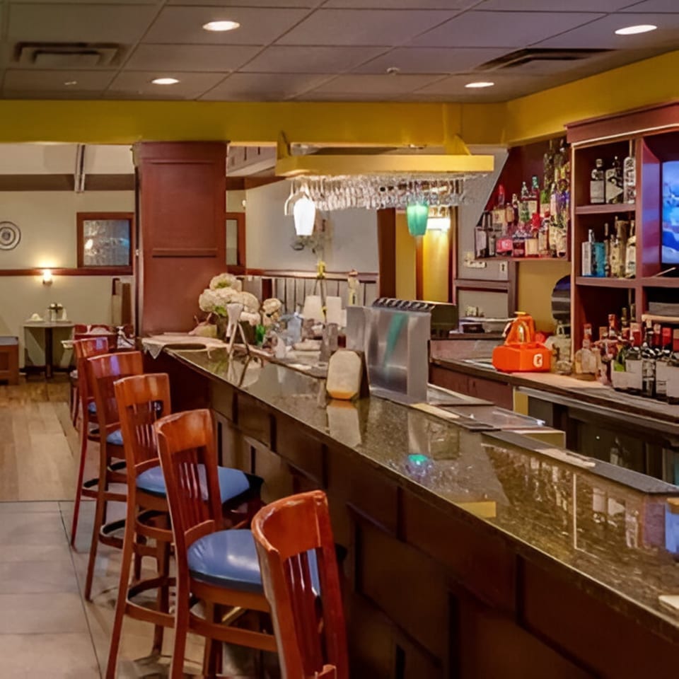 A long, dark bar with several wooden stools and a fully stocked liquor shelf at Taste of Awadh.