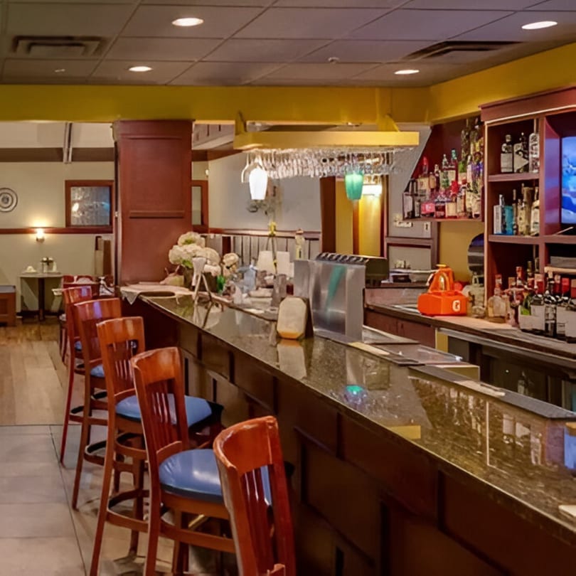 A long, dark bar with several wooden stools and a fully stocked liquor shelf at Taste of Awadh.