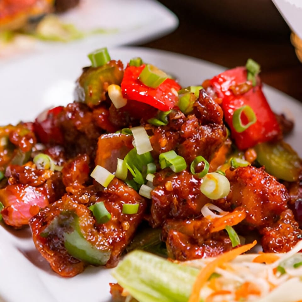 Close-up of Indian chili chicken, garnished with red and green bell peppers and spring onions.