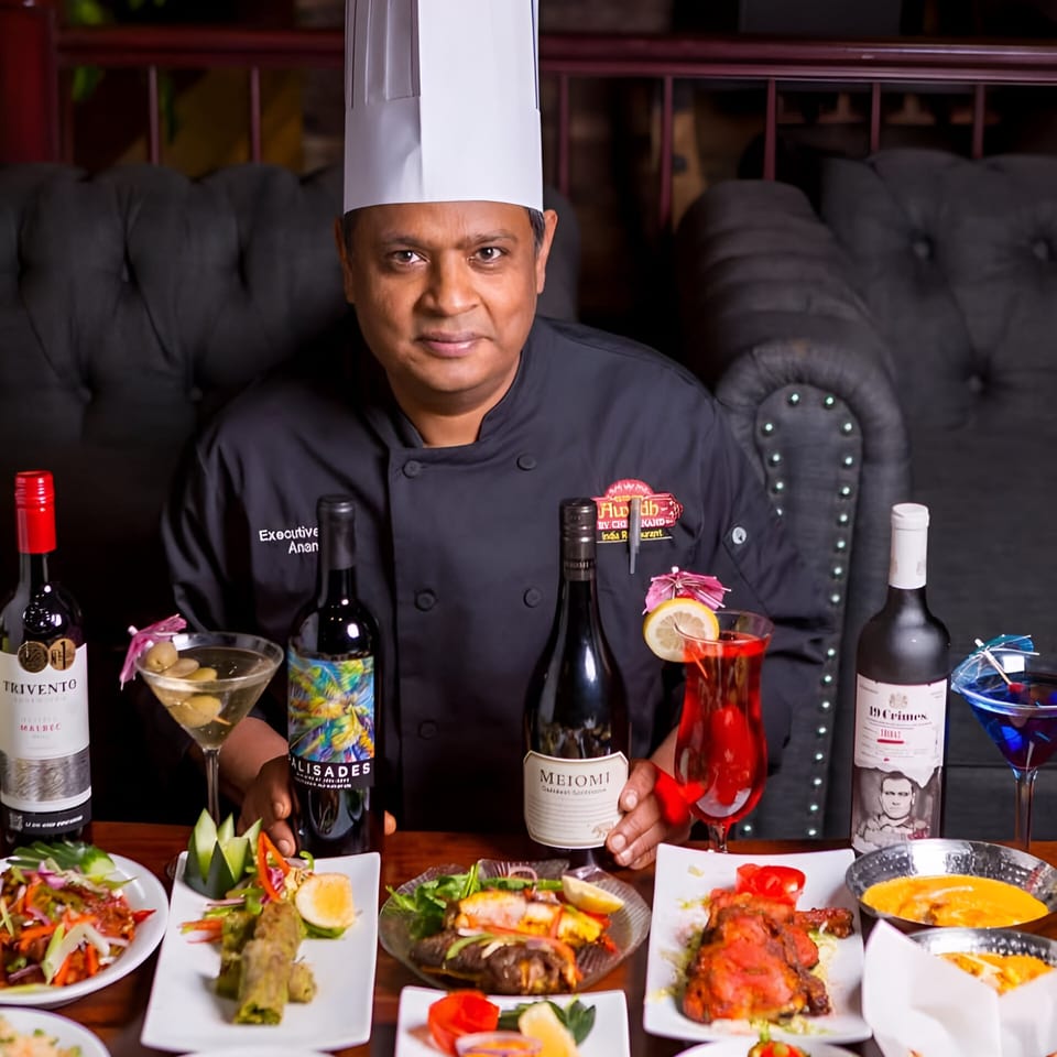 Chef Anand poses with a spread of Indian dishes, wines, and cocktails at Taste of Awadh.