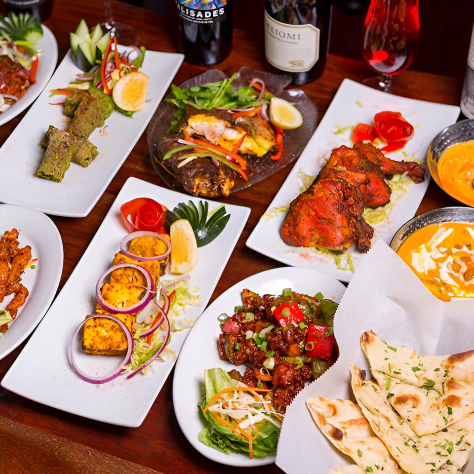 A table laden with various Indian dishes, including tandoori chicken, paneer, curries, and naan bread.