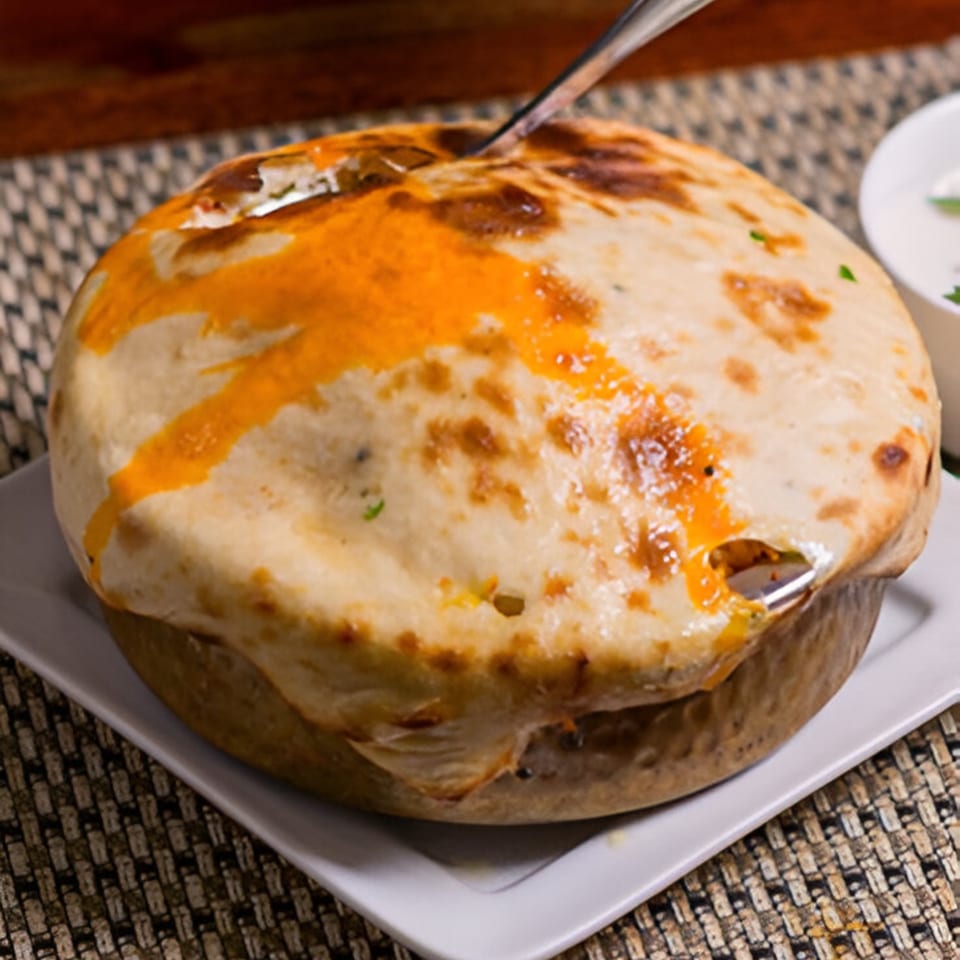 A golden-brown Indian dum biryani, sealed with dough, with a spoon breaking through the crust.