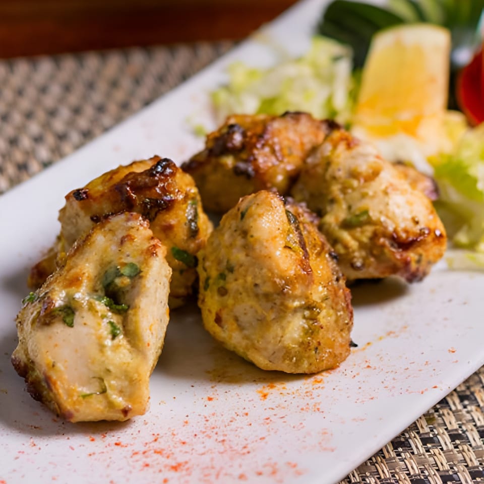 Close-up of five pieces of Indian chicken tikka with a side of salad and lemon.
