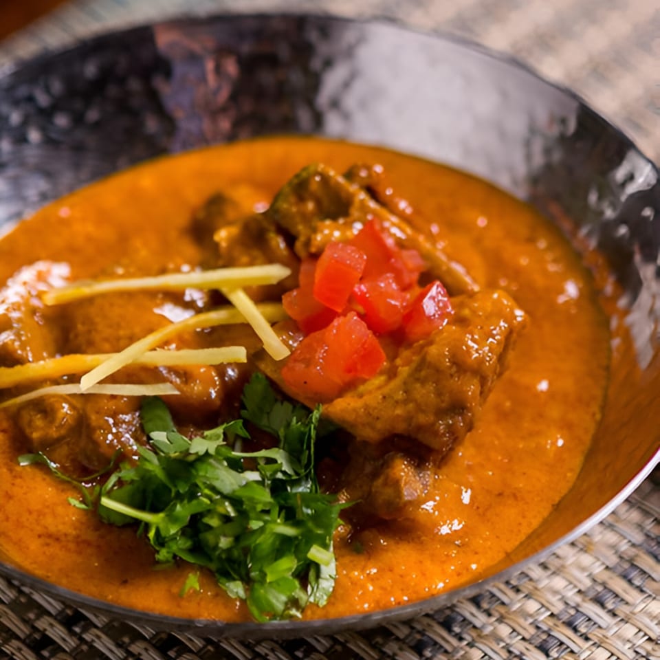 Indian curry with meat, garnished with fresh cilantro, diced tomatoes, and ginger slivers.